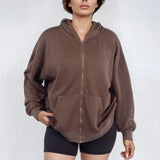 Woman wearing a relaxed brown full zip French Terry hoodie and black shorts on a white background